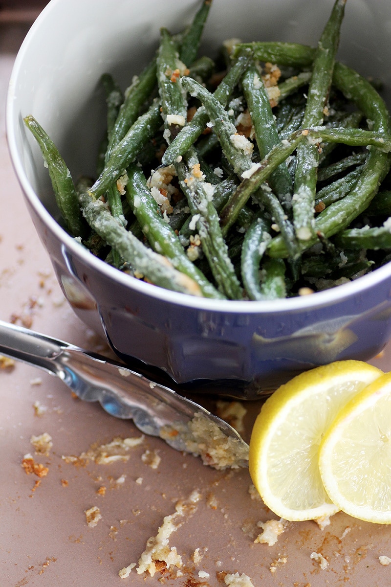 green beans in blue bowl sitting on pink pan with lemons