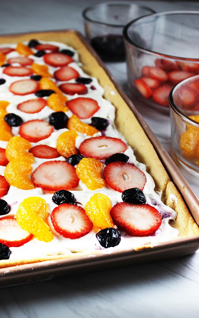 fruit pizza with bowls of strawberries, oranges, and blueberries