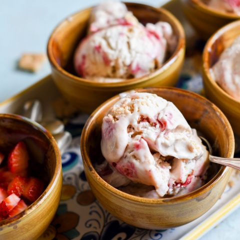Three bowls of strawberry cheesecake no churn ice cream on a tray with a bowl of strawberries