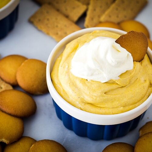 pumpkin dip in a bowl topped with whipped cream surrounded by cookies and graham crackers