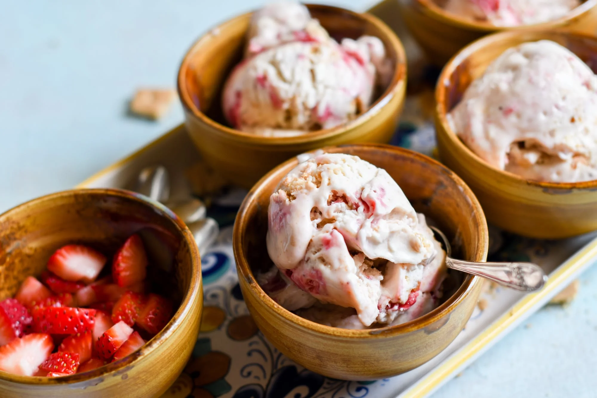 Three bowls of strawberry cheesecake no churn ice cream on a tray with a bowl of strawberries